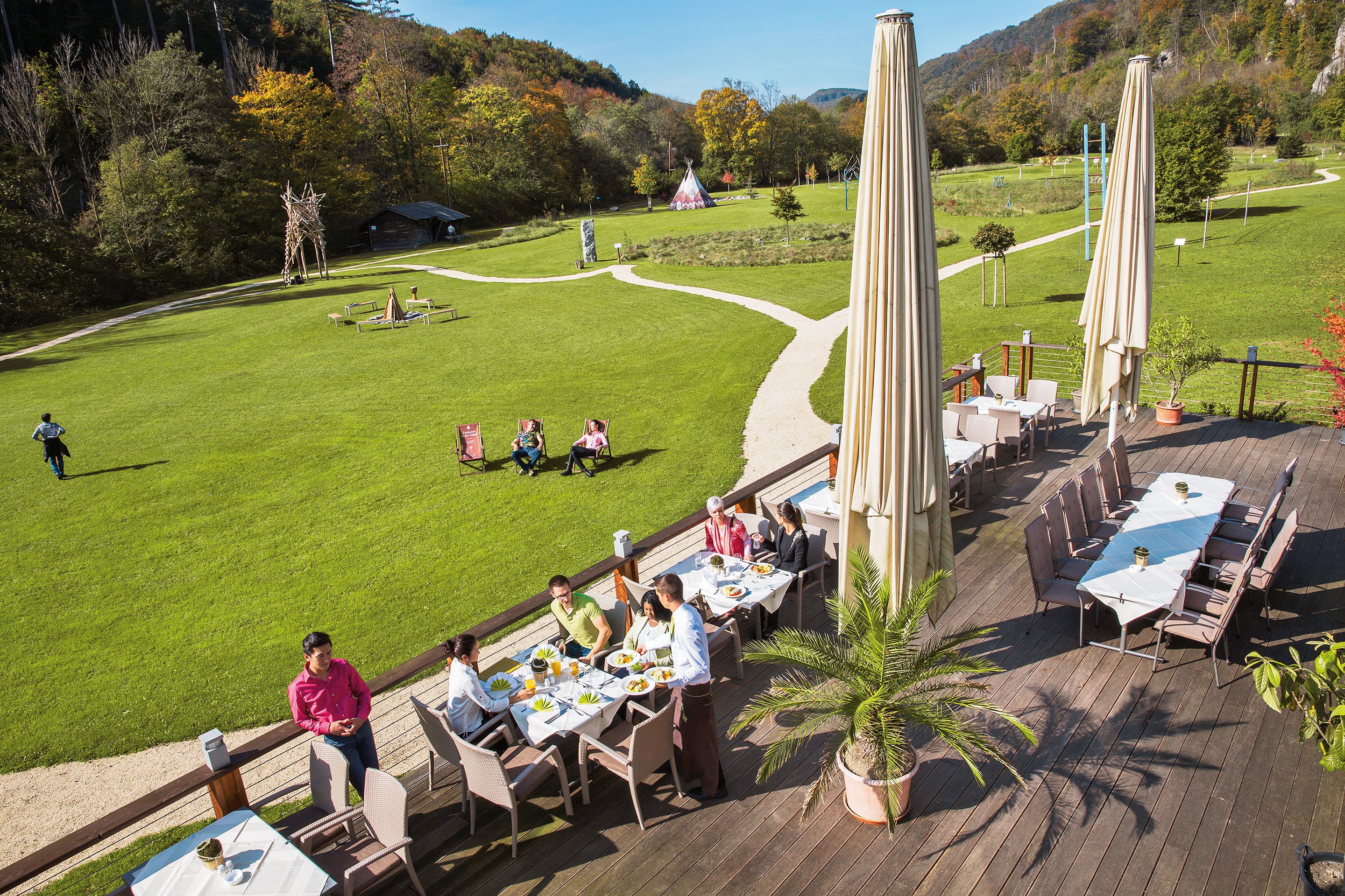 Terrace of the seminar and event hotel Krainerhütte with guests eating, surrounded by green meadows and forest.