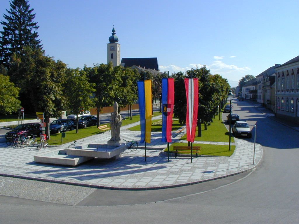 Square in Ruprechtshofen with church, statues and flags.