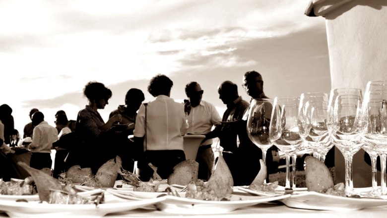 People at an outdoor event with wine glasses and snacks on a table.