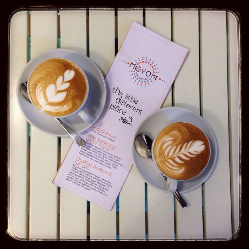 Two cappuccinos with latte art and a flyer on a table.