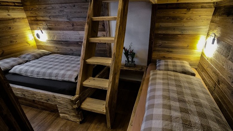 Interior view of a rustic wooden hut with two beds and a wooden ladder.