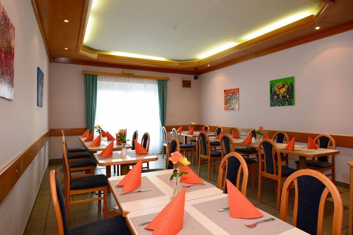 A dining room with laid tables, orange napkins and vases of flowers.