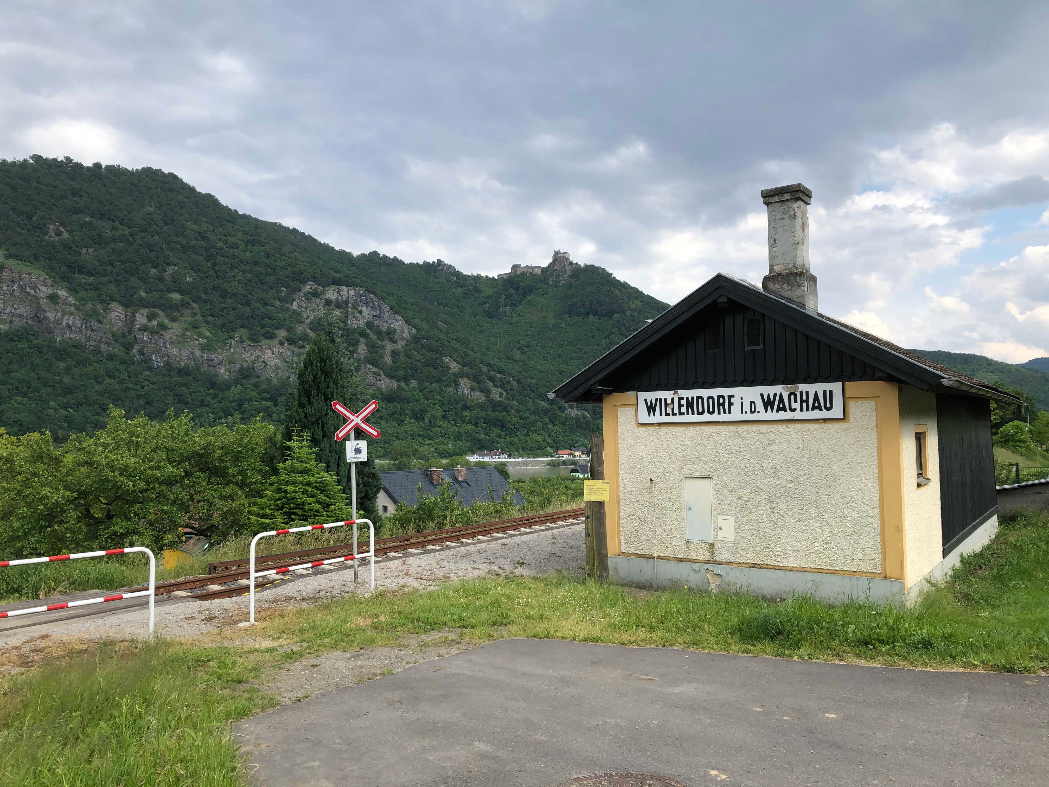 Small station building in Willendorf in the Wachau, surrounded by green hills and railroad tracks.