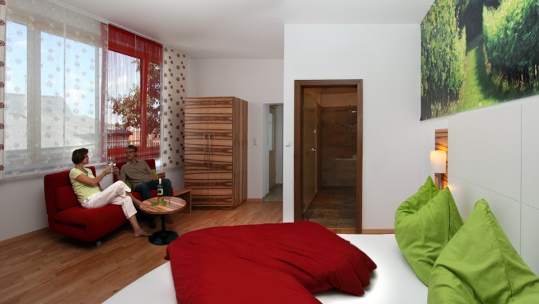 Modern guest room with red sofa, green-red bed and large window.