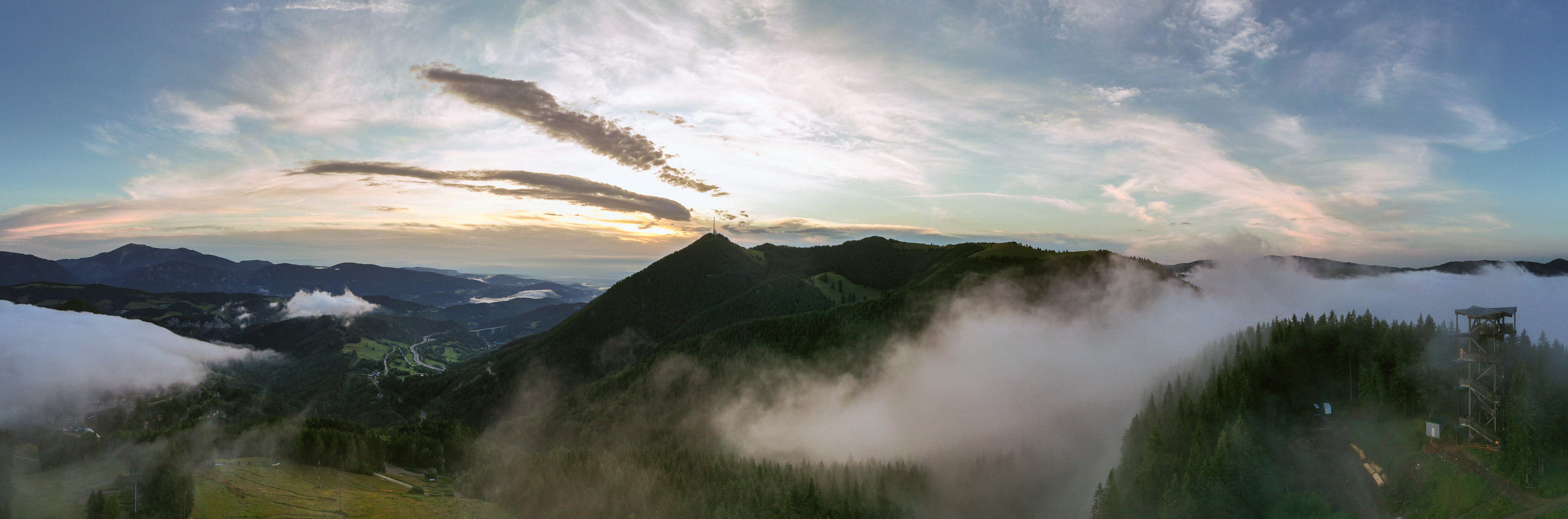 Panoramic view of the Sonnwendstein at sunrise with fog and a lookout tower in the foreground.