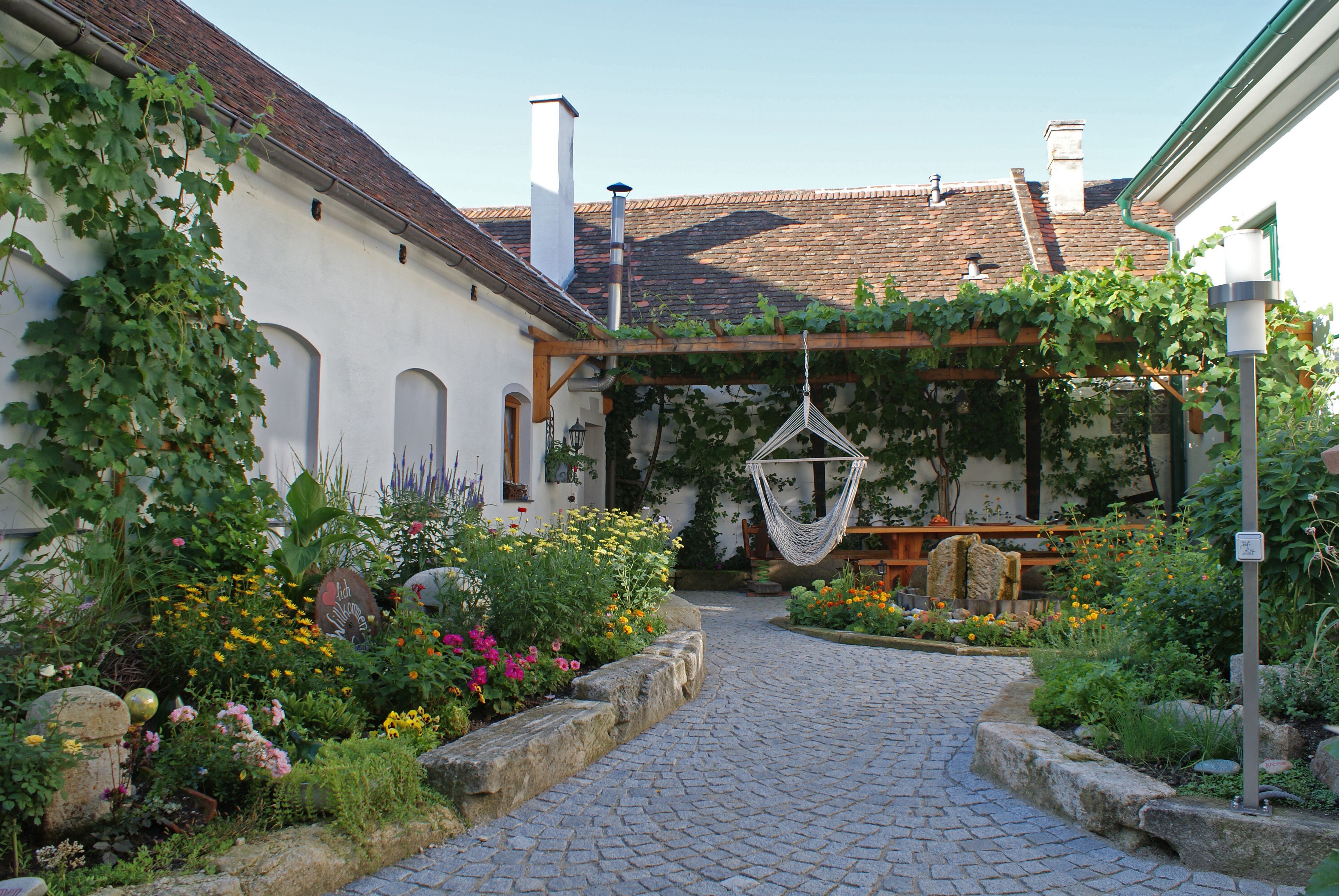 An idyllic courtyard with flower beds, a hammock and a covered seating area.