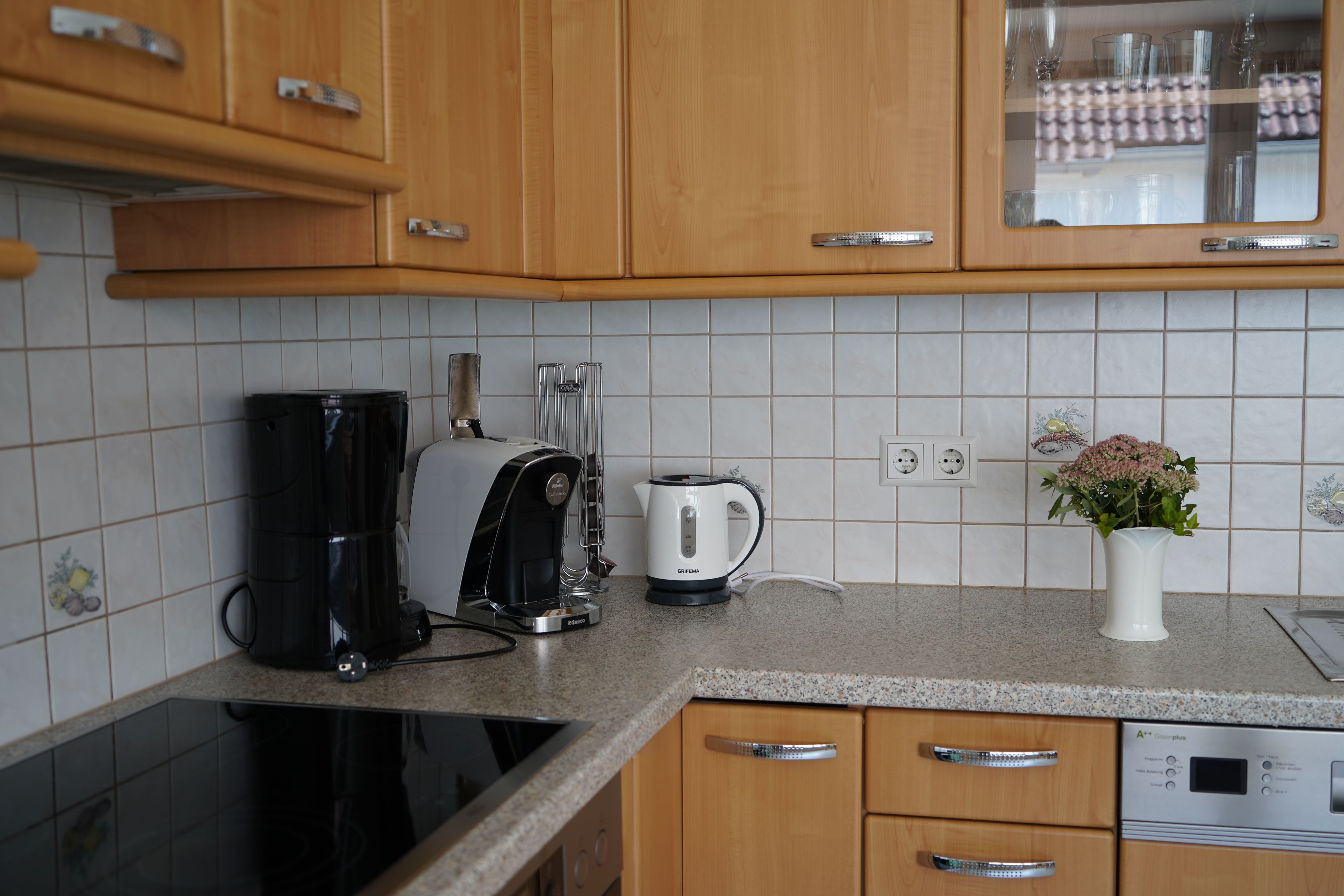 Kitchen corner with coffee machine, kettle and vase on worktop.