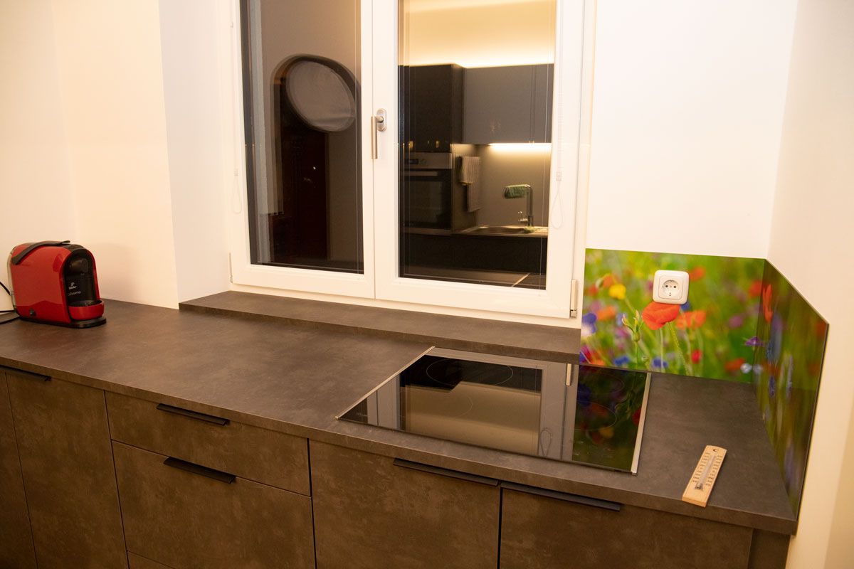Modern kitchen with induction hob, red coffee machine and colorful floral splashback.
