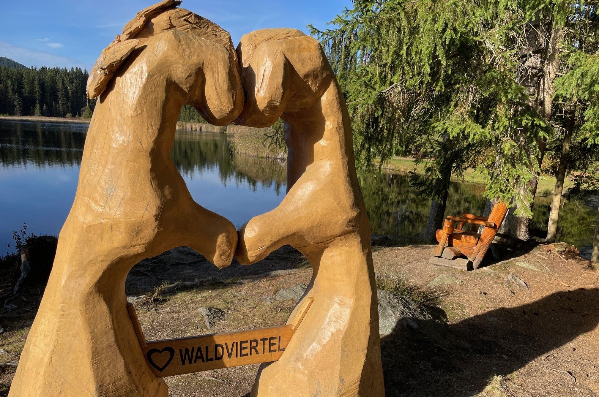 Wooden sculpture of two hands forming a heart with the inscription 'Waldviertel' in front of a lake and forest.