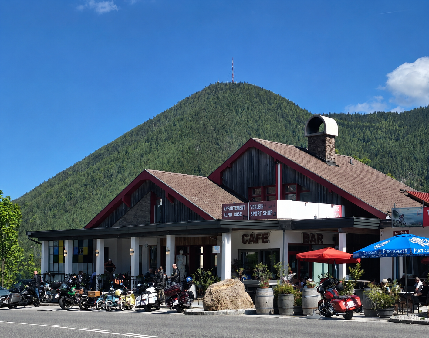 A café and bar with motorcycles in front, surrounded by mountains and trees.