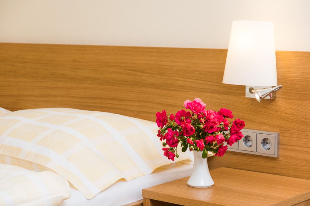 A guest room with a bed, a bedside lamp and a bouquet of flowers in a vase on the bedside table.