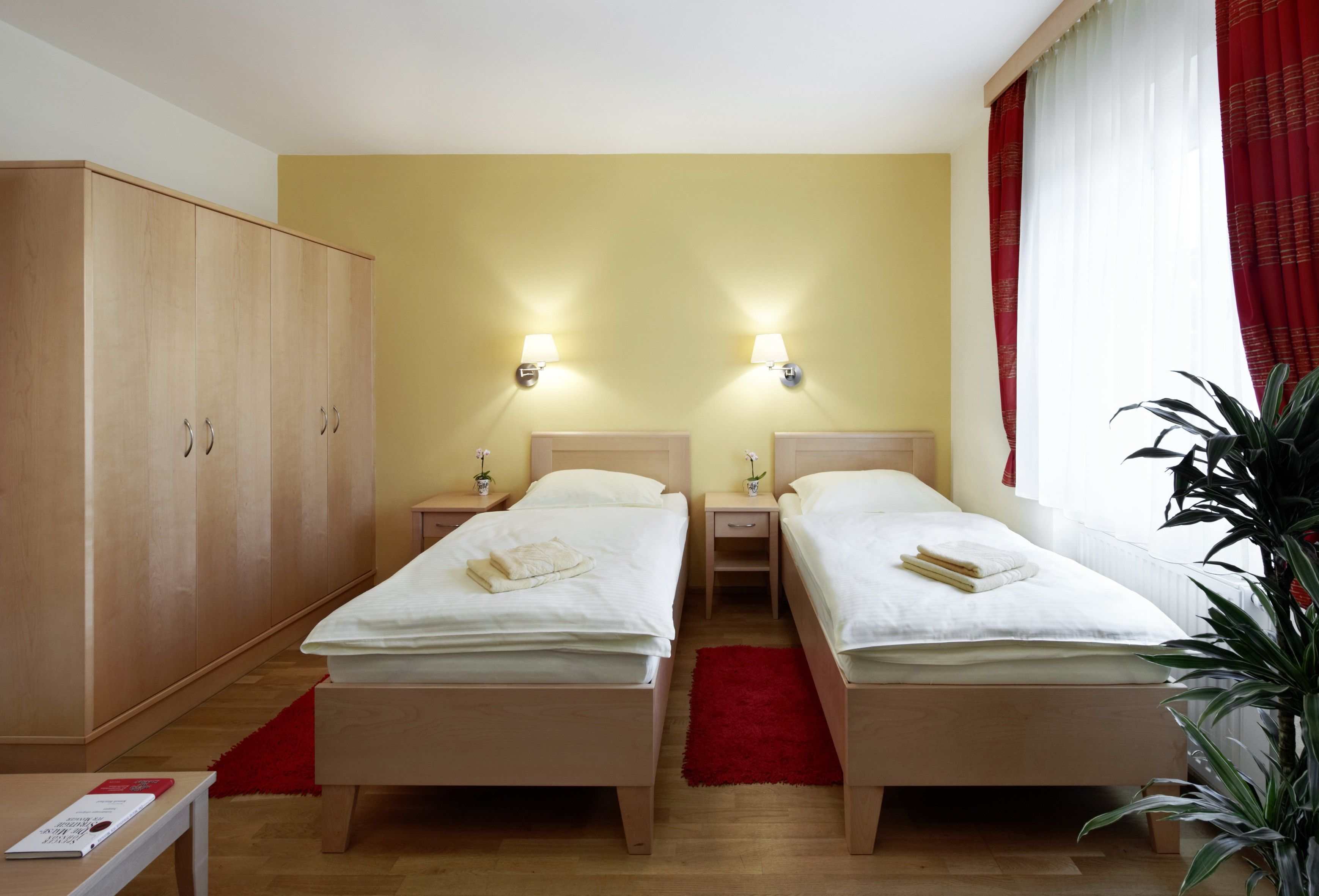 A guest room with two single beds, a large closet, red curtains and a plant.