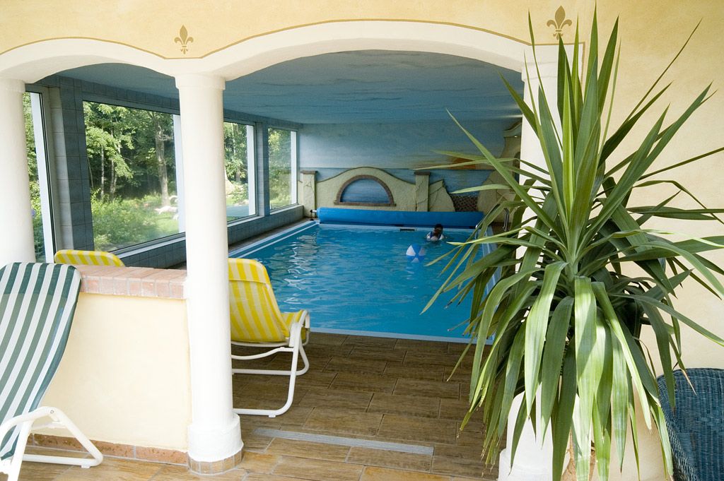 Indoor pool with sun loungers and plants, view to the outside.