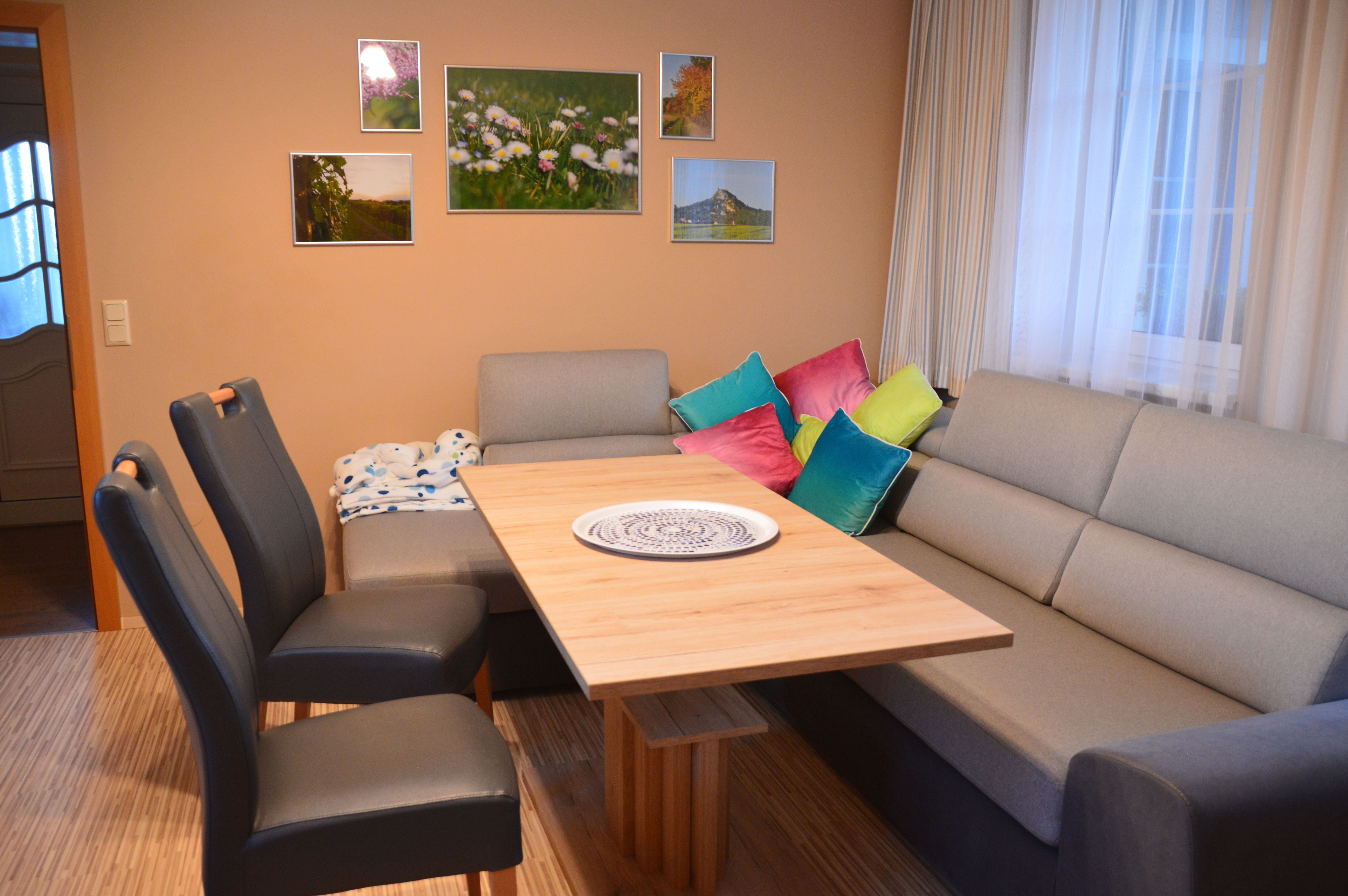 Living and dining area with grey sofa, wooden table, colorful cushions and murals.