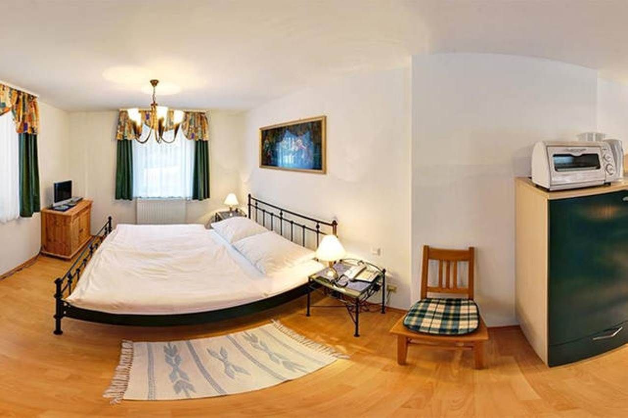 Small bedroom with double bed, bedside tables, TV, microwave and chair.