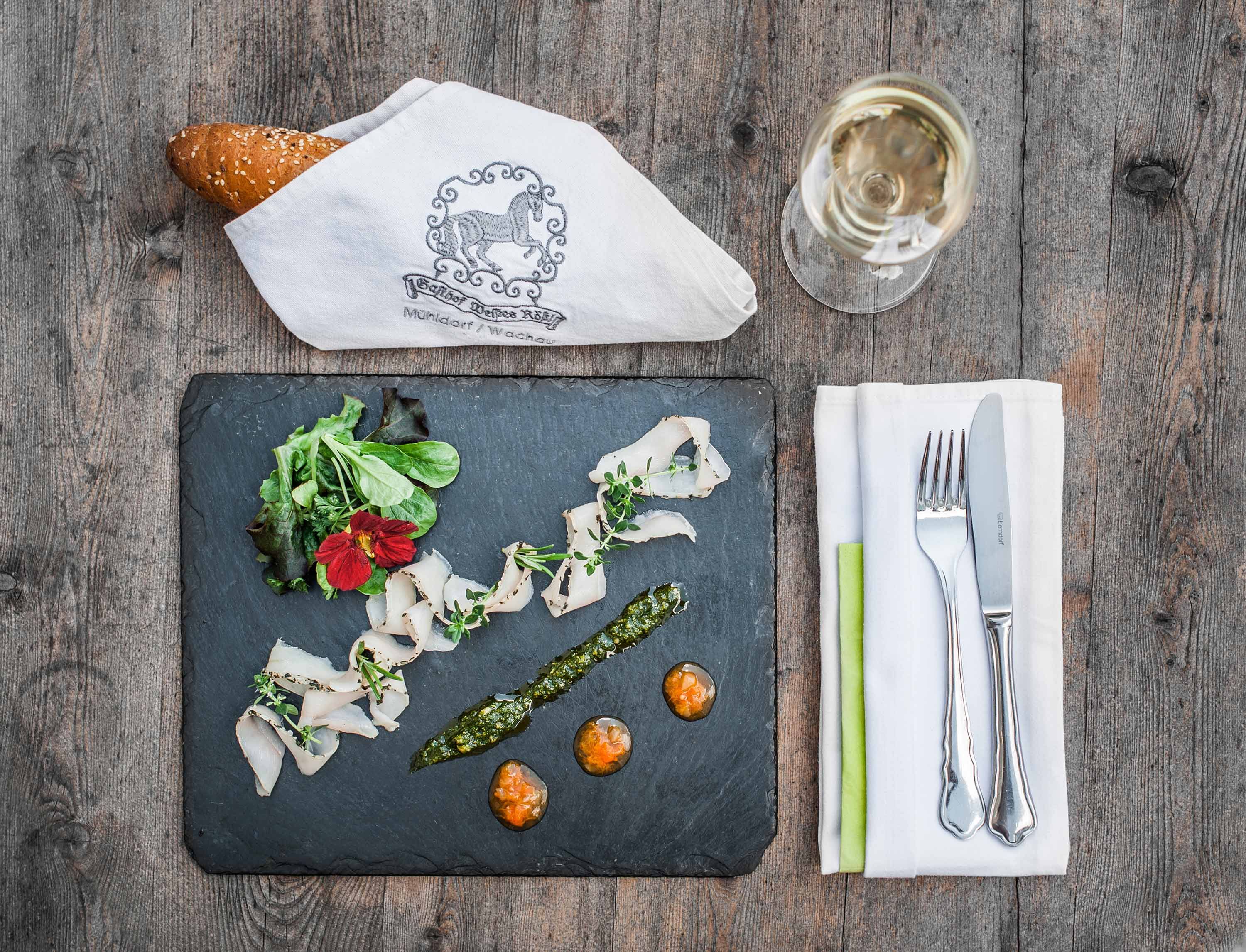 Elegant starter on a slate plate with bread, cutlery and wine glass on a wooden table.