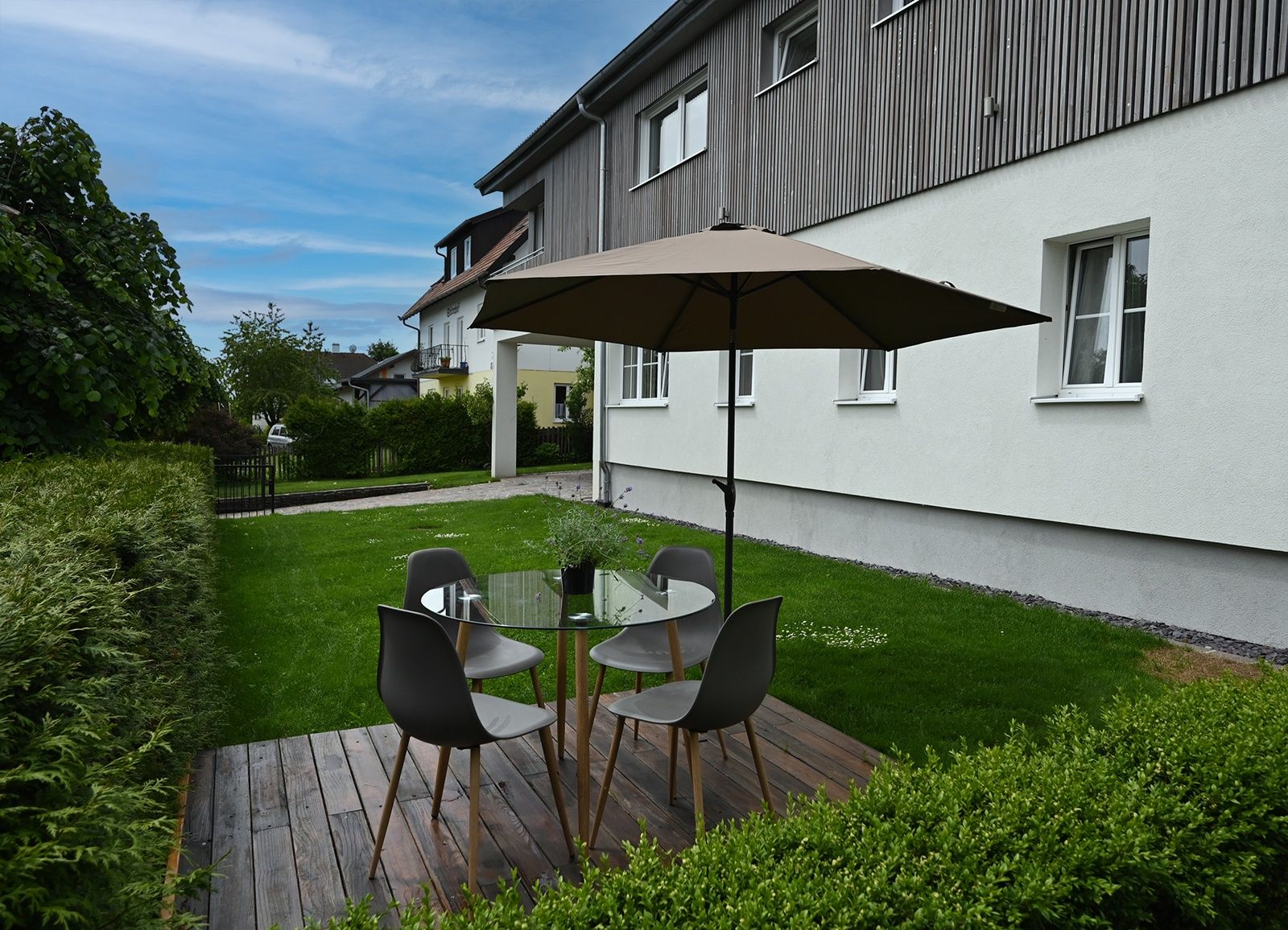 Garden with seating area, table, chairs and parasol on wooden terrace.