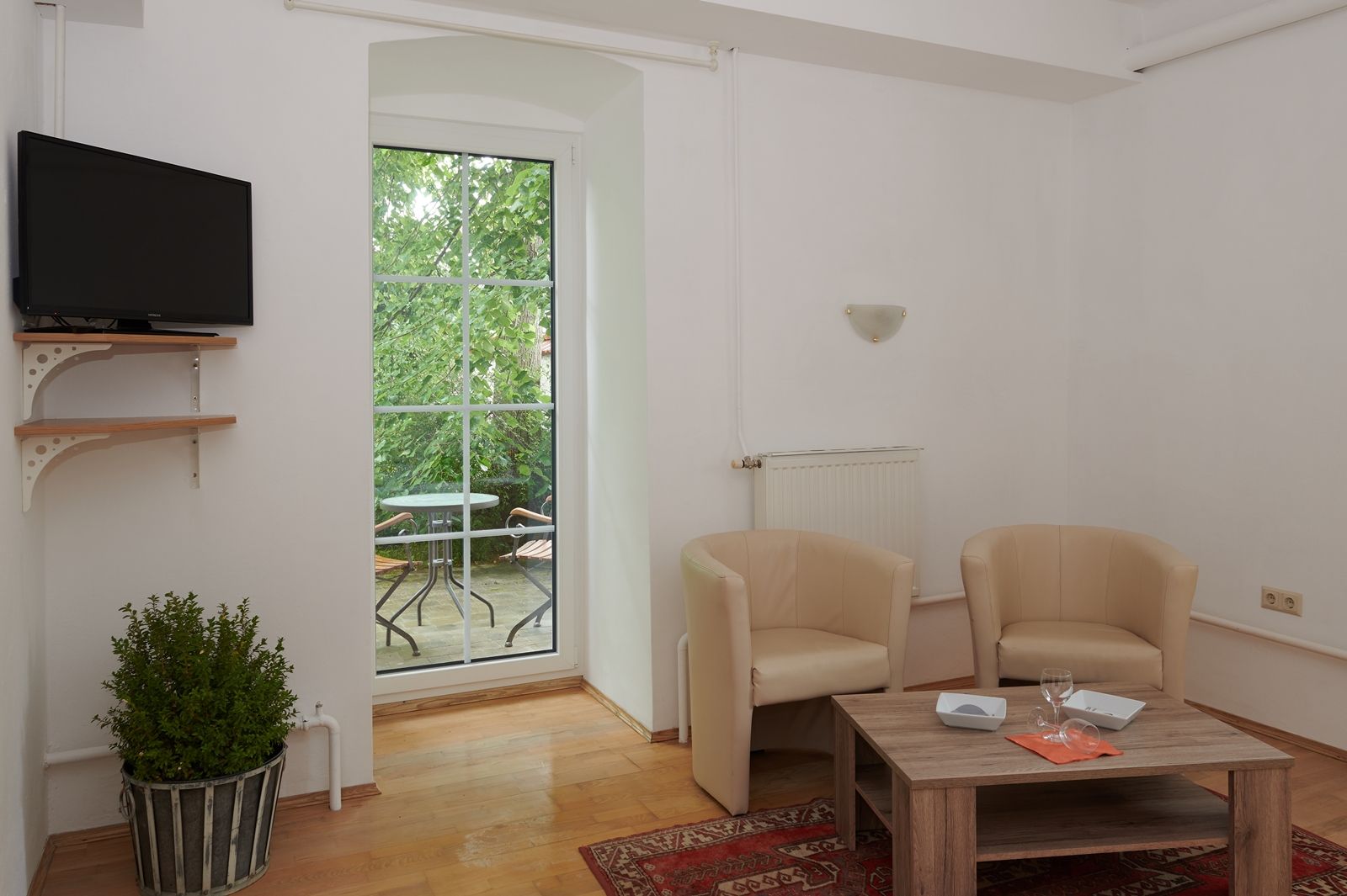 Living room with two beige armchairs, wooden table, TV and balcony with table and chairs.
