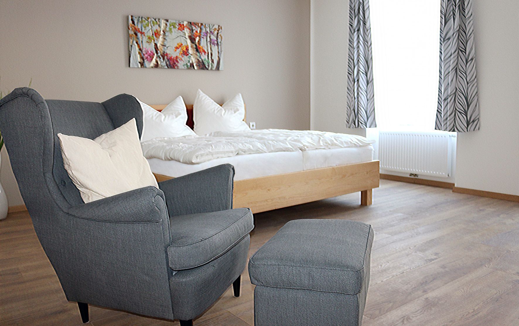 Gray, comfortable chair in the foreground. A double bed with white bed linen in the background.
