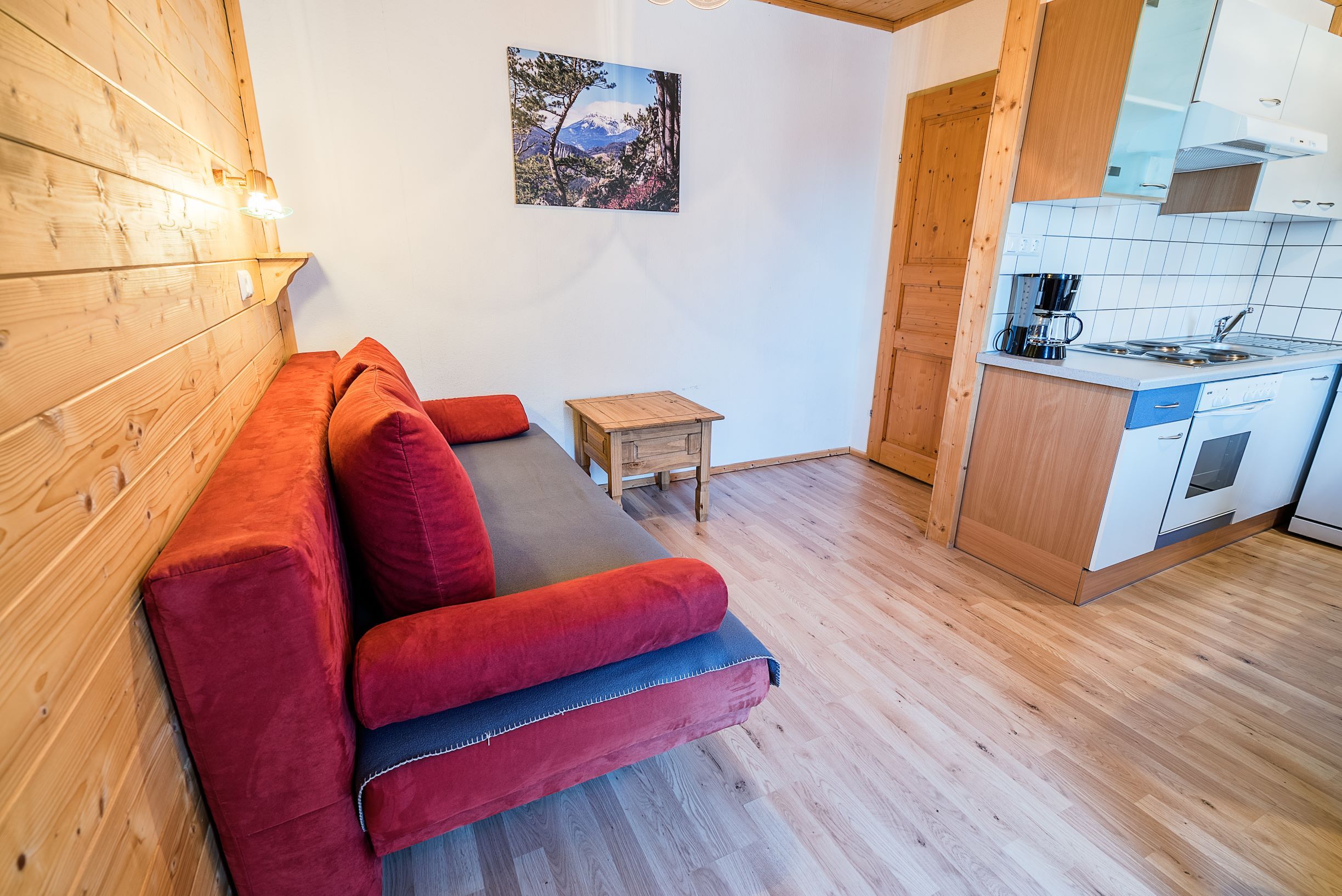 Living room with red sofa, wooden walls and small kitchen.
