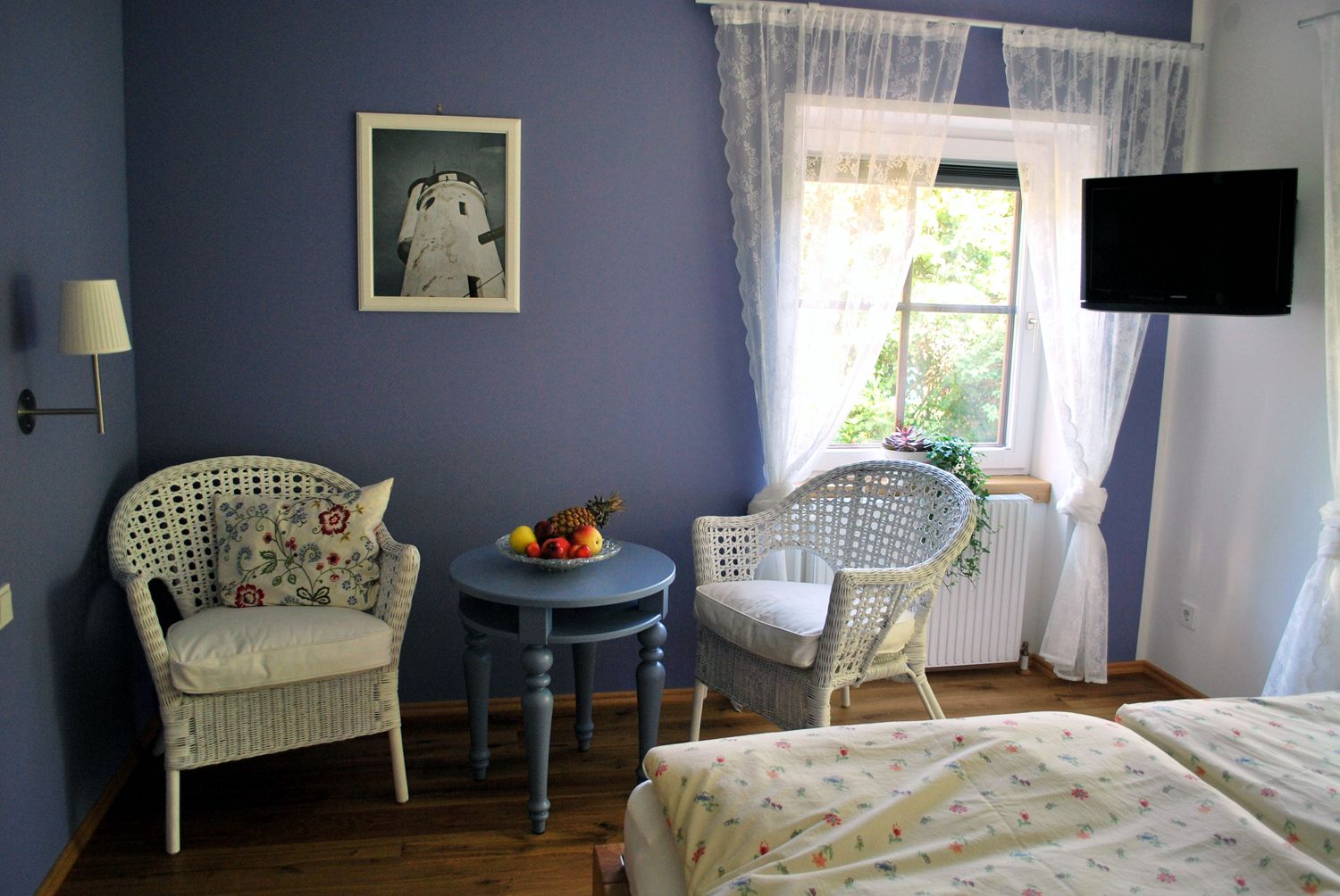 Cozy room with blue walls, two wicker armchairs, a round table with a fruit bowl and a window with white curtains.