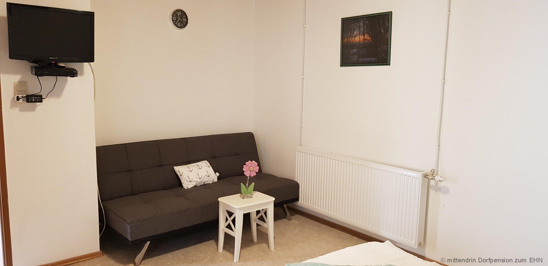 TV on the wall, next to it a gray sofa and a small table.