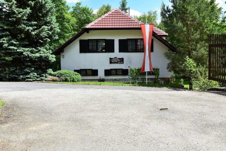 A white house with a red roof and an Austrian flag in front of it, surrounded by trees.