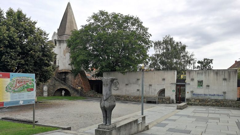 Town wall and museum in Horn with statue and information board in the foreground.