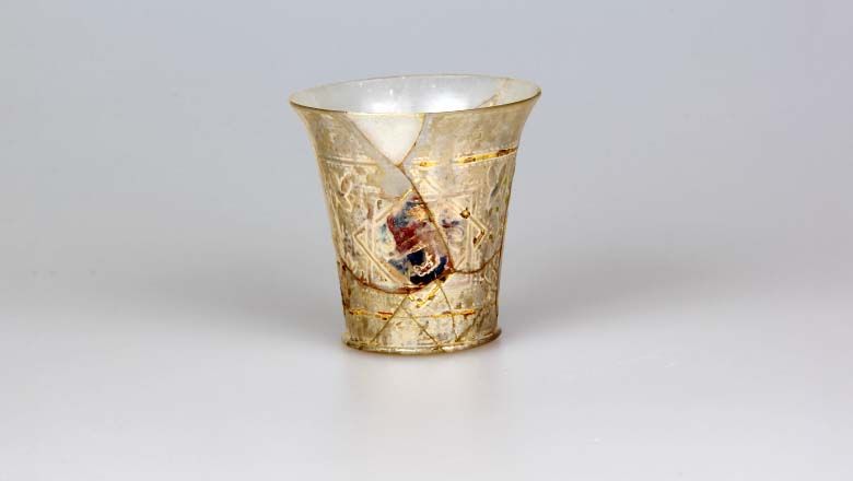 Antique glass beaker with decorations on a light background.