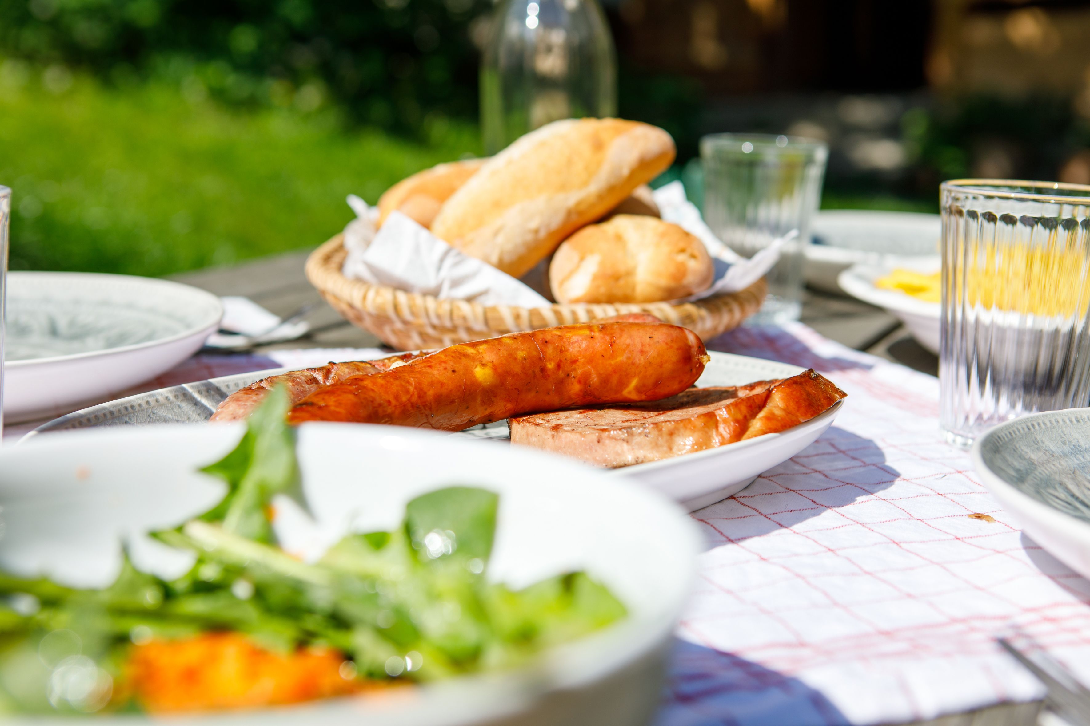 An outdoor table with bread, sausage, and salad.
