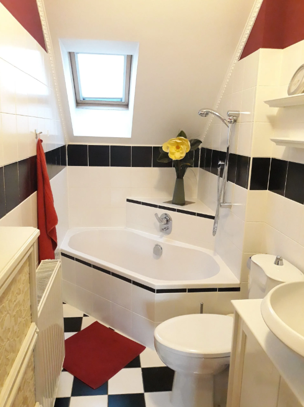 Bright bathroom with corner bath, skylight and black and white tiles.