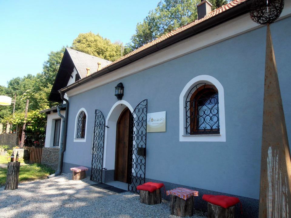 A small, blue building with a wooden door and decorative bars in front of the windows. In front of it are wooden stools with red cushions.
