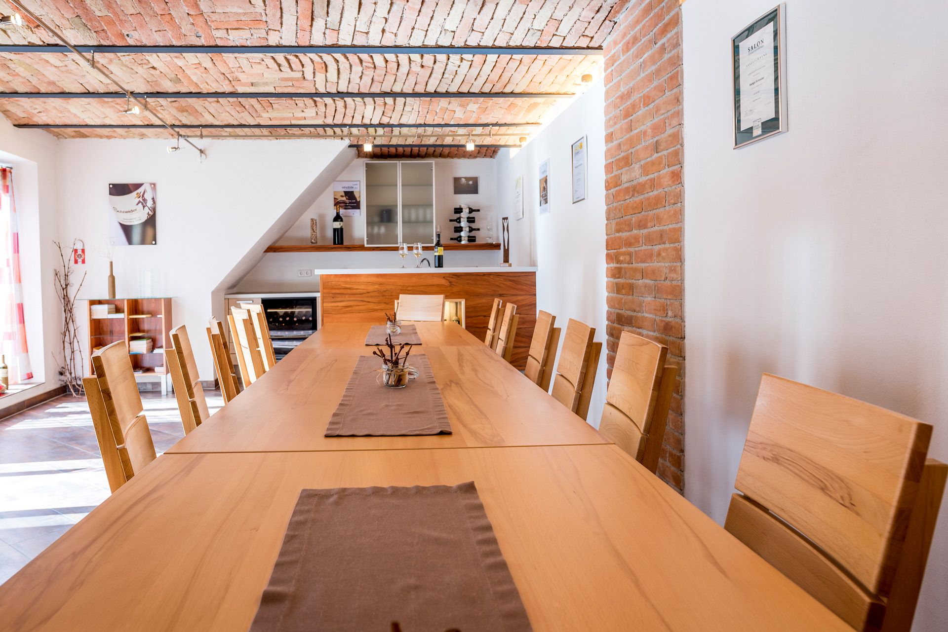 Tasting room with long wooden table and chairs, brick ceiling and wine rack.
