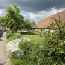 Rural scene with a cloudy sky, green meadow and a building with a red tiled roof.