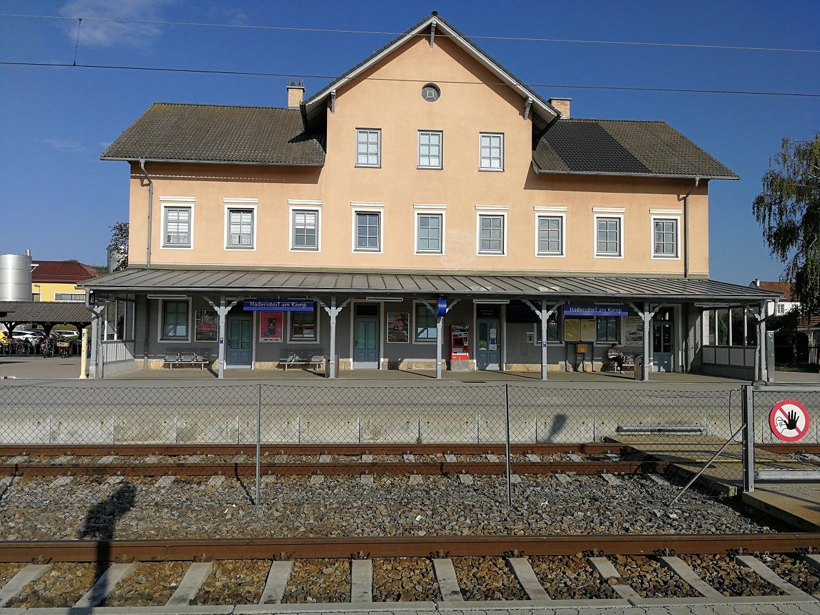 Hadersdorf am Kamp station with tracks in the foreground and a yellow building in the background.