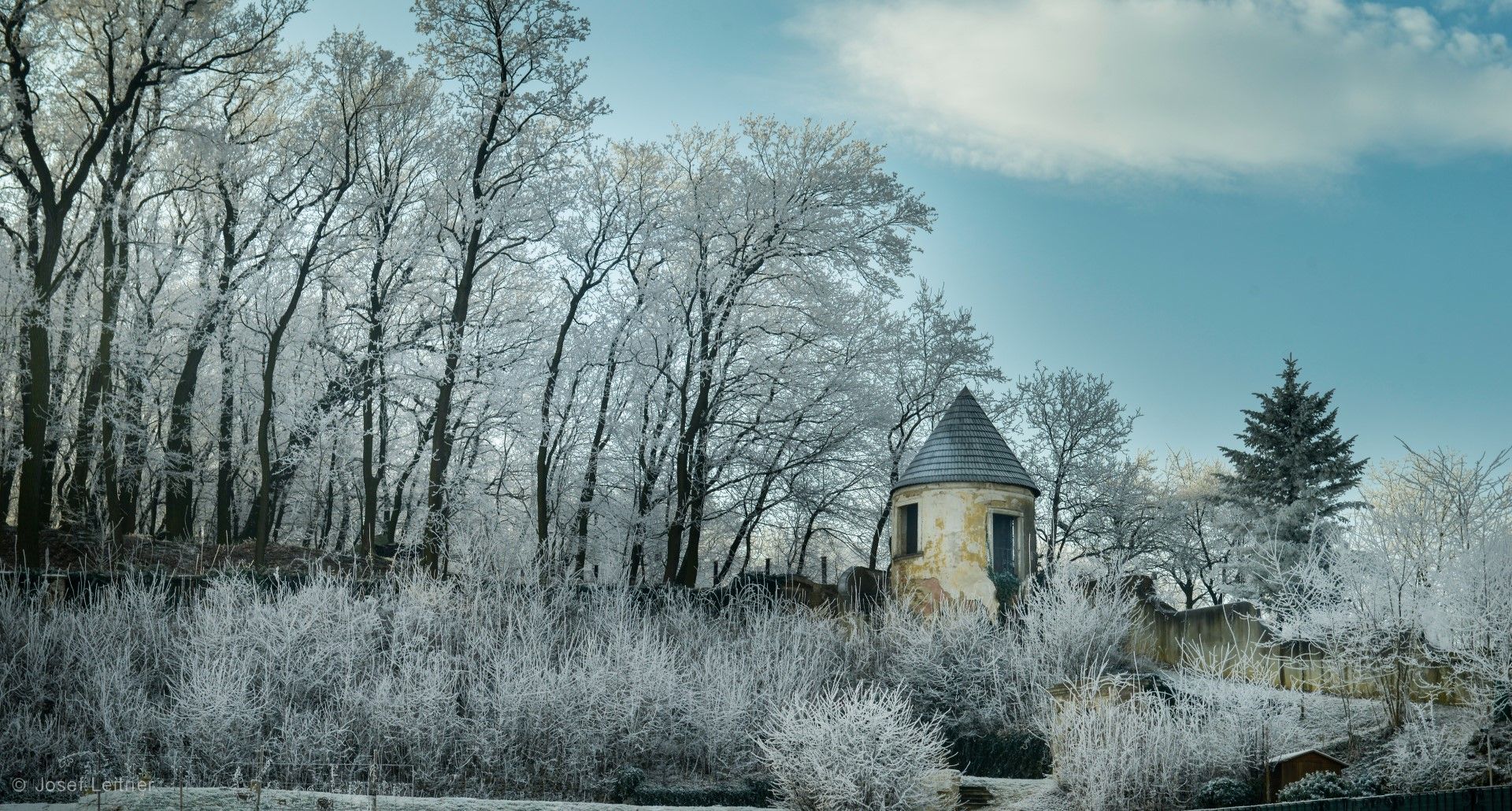 An old tower stands in a snowy landscape, surrounded by trees covered in hoarfrost.