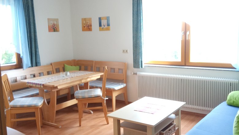 Bright living room with wooden furniture, corner bench, table, sofa and large windows with blue curtains.