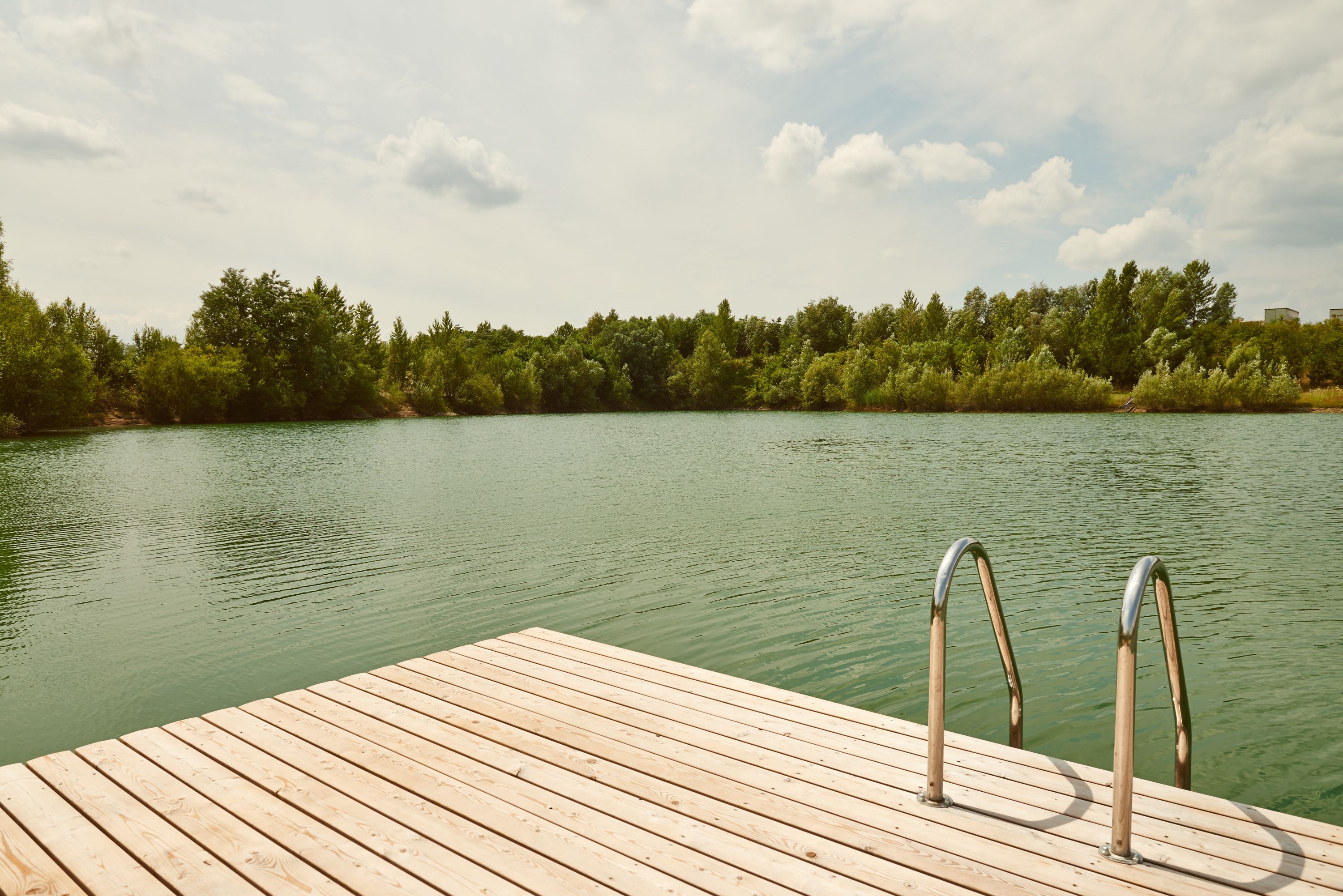 Wooden footbridge with ladder at the Persenbeug-Gottsdorf bathing pond, surrounded by trees.
