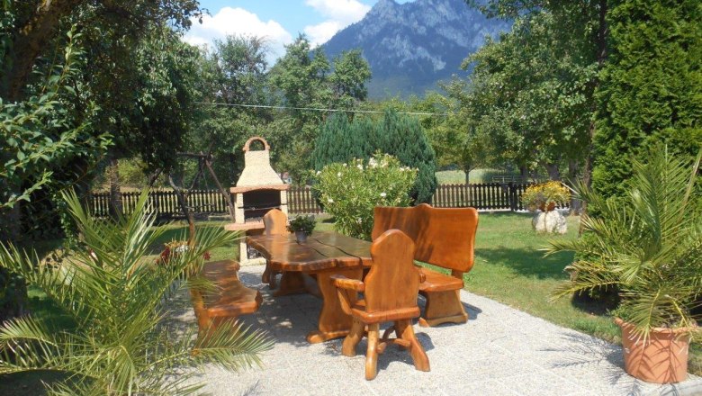 Garden area with wooden furniture and barbecue against a mountain backdrop.