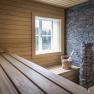 Interior view of a sauna with wood paneling, a window, a bucket and a stove with stones.