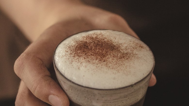Close-up of a hand holding a glass with cappuccino and milk foam.