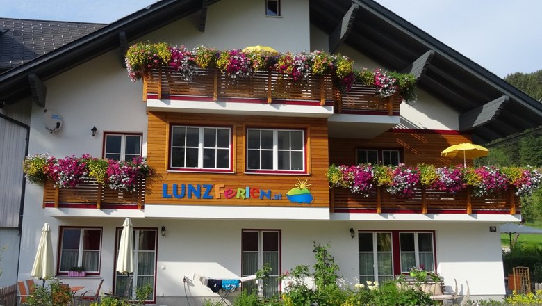A vacation home with colorful flowers on the balconies and the lettering 'LUNZ Ferien'.