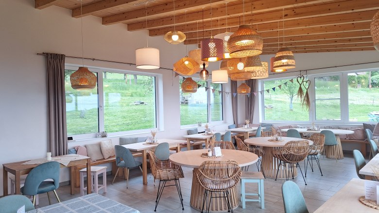 Cozy dining room with wooden furniture and hanging lamps, large windows with a view of the greenery.