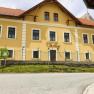Yellow building with the inscription 'Villa Luef', surrounded by a fence and a road in the foreground.