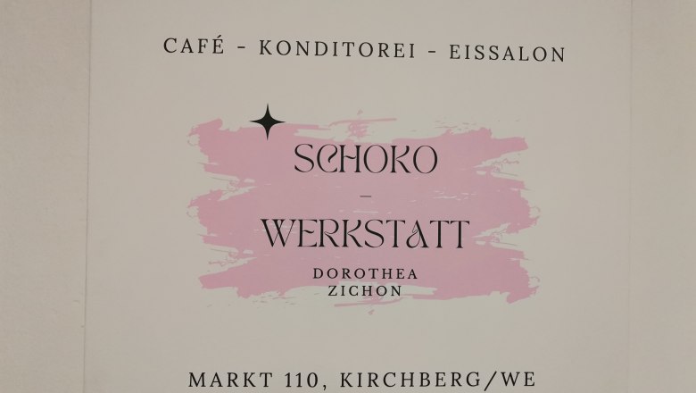 Sign for the chocolate workshop in Kirchberg with a pink background.