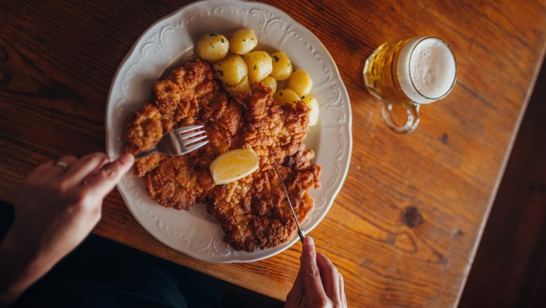 Plate with schnitzel, potatoes and lemon, next to a glass of beer.