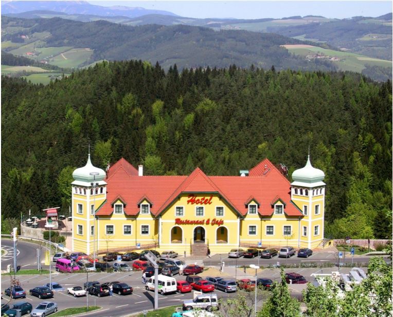 Yellow hotel with red roofs in a green, hilly landscape.
