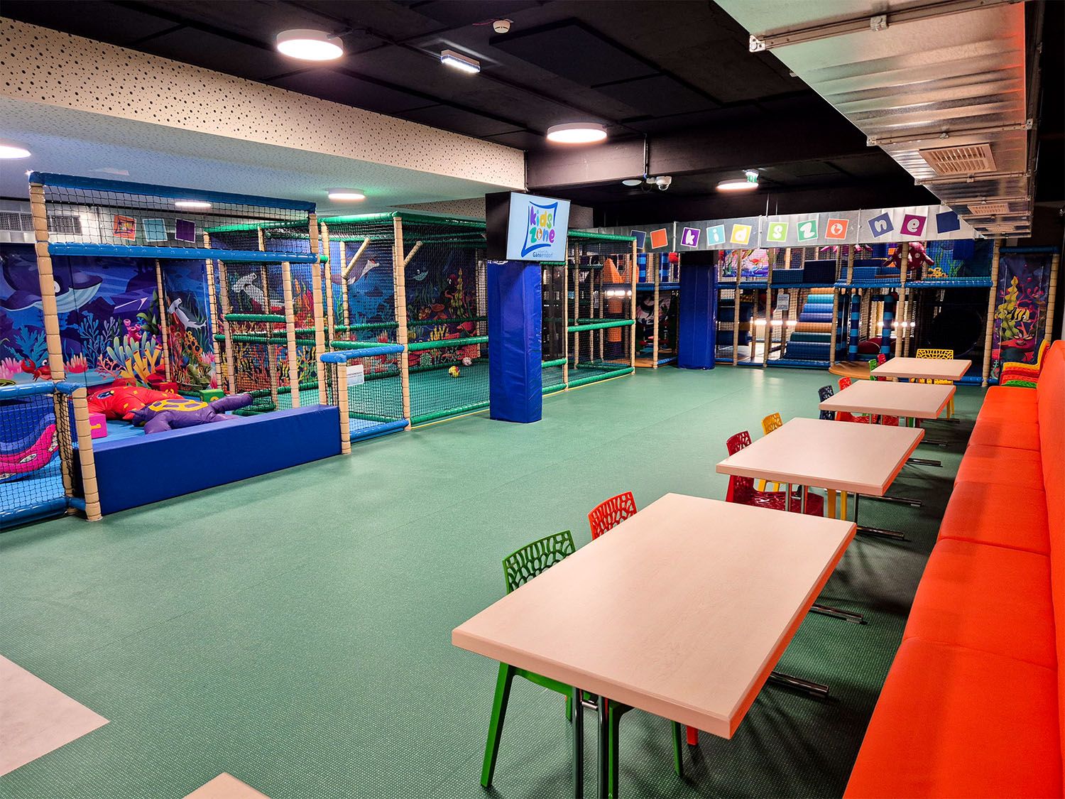 Interior view of a colorful indoor playground with climbing frames and tables.