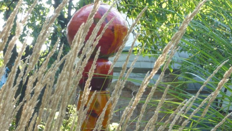 Colorful sculpture in the garden behind grasses and plants.