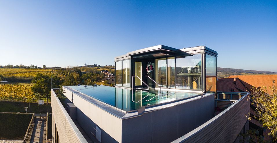 Rooftop pool with glass walls on a modern building surrounded by countryside.